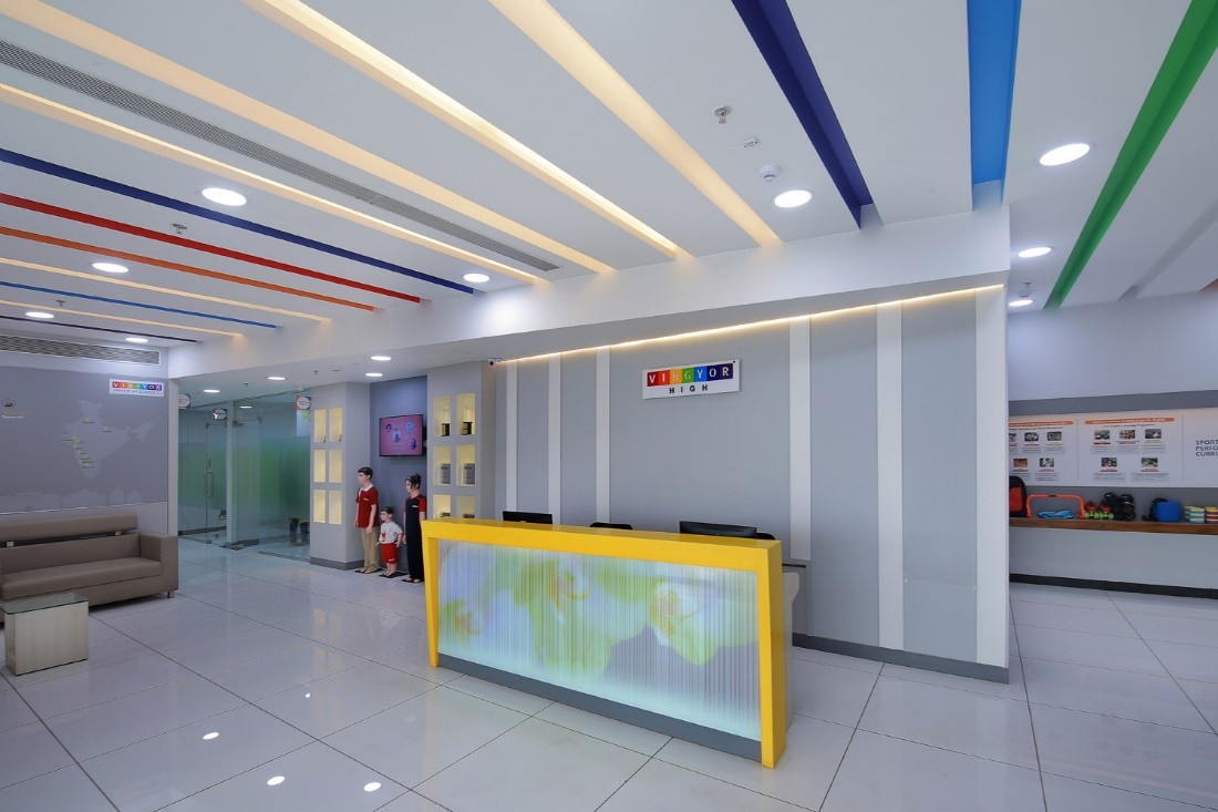 Vibgyor High School reception area with a yellow desk and colourful ceiling accents